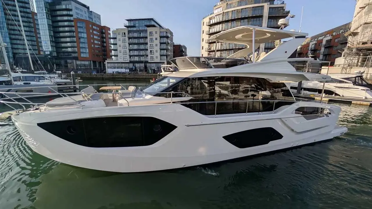 Large white luxury motor yacht moored in a city marina, with modern apartment buildings in the background.