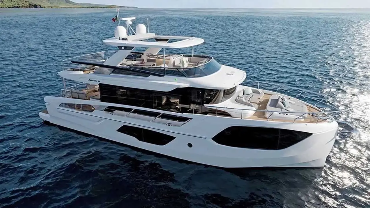 White luxury motor yacht on blue sea, viewed from above, with a rocky coastline in the background.