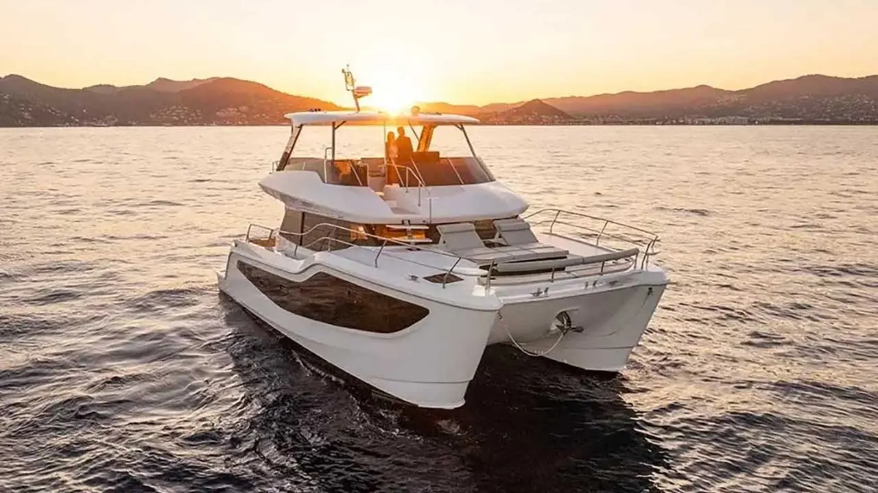 White luxury catamaran cruising at sunset, with two people aboard and mountains in the background.