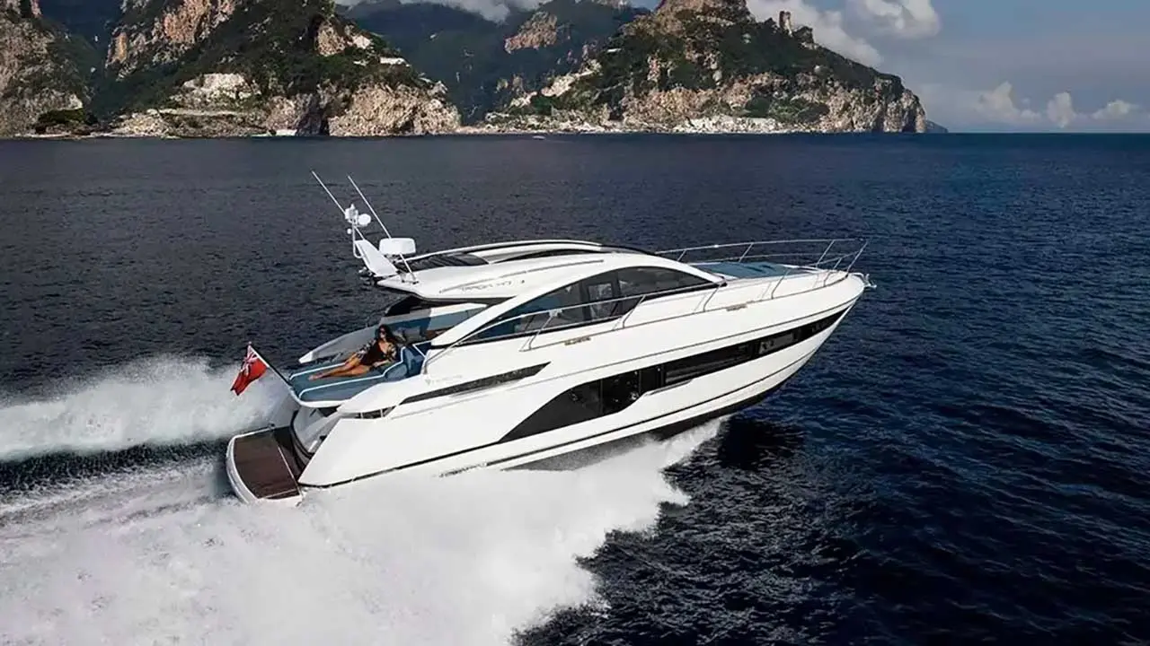 Luxury white motor yacht speeding past a rugged Mediterranean coastline, leaving a foamy wake.