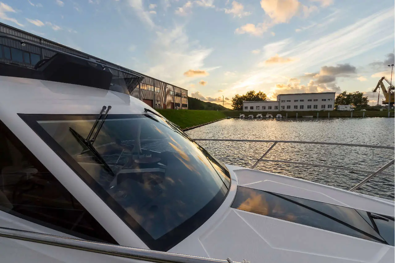A yacht is docked near a modern building at sunset, with reflections on the water and scenic clouds in the sky.