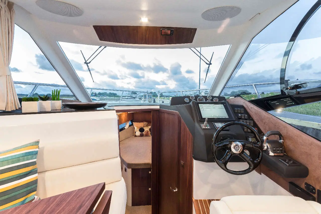 Luxury yacht interior featuring a steering wheel, navigation controls, and scenic views through large windows.