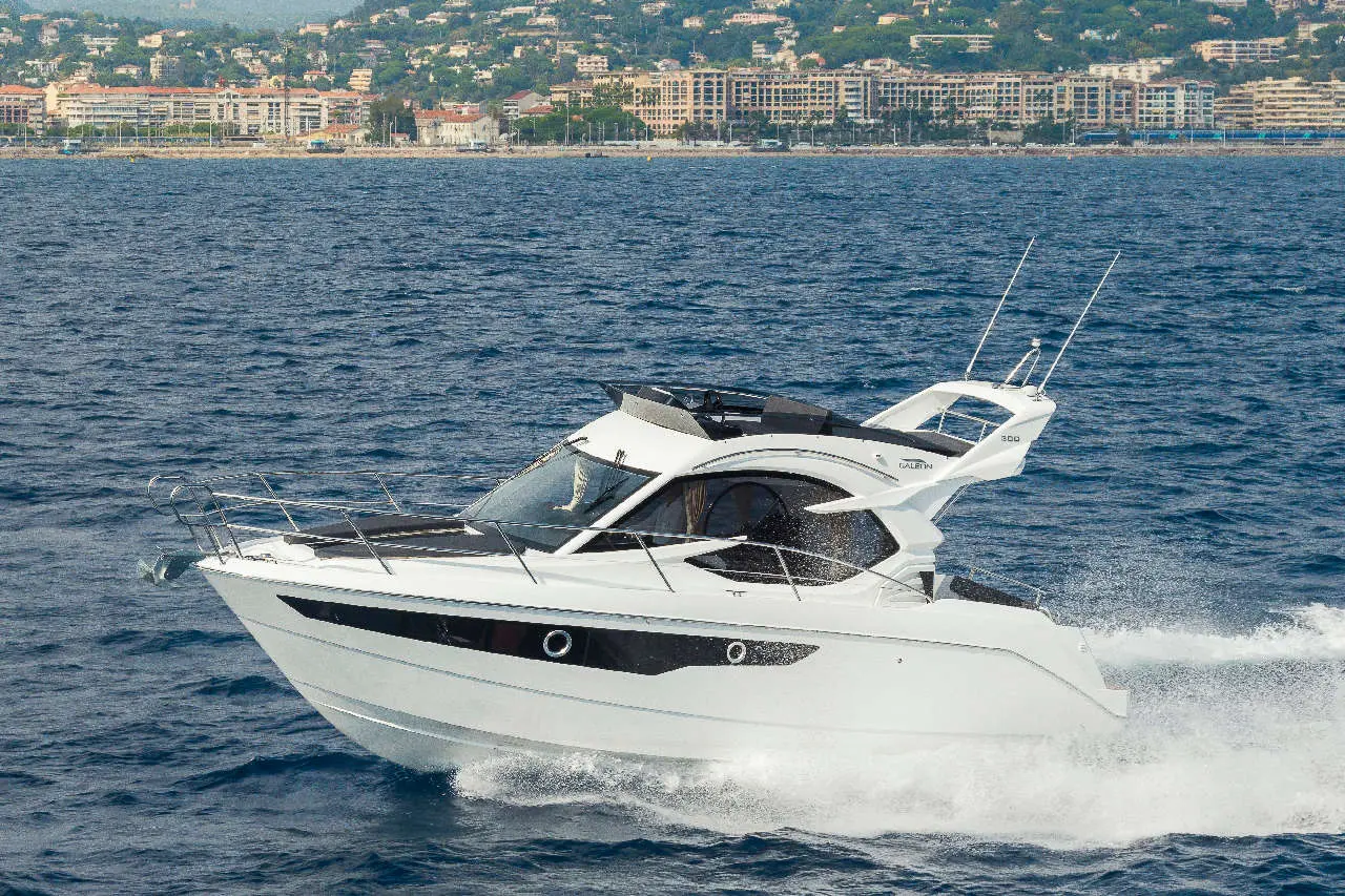 A sleek white motorboat speeds through deep blue waters, with coastal buildings visible in the background.
