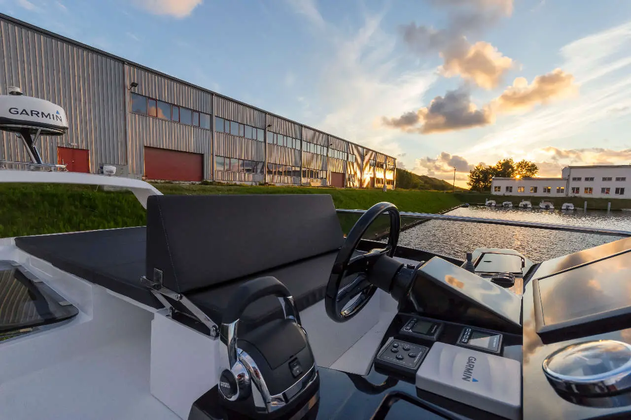 View from a boat cockpit showcasing a Garmin display, with a marina and industrial buildings at sunset in the background.