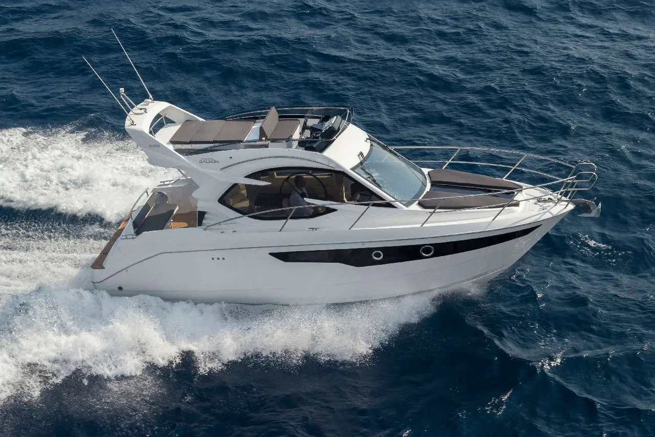 A white luxury yacht navigates through deep blue ocean waters, leaving a trail of foam in its wake.