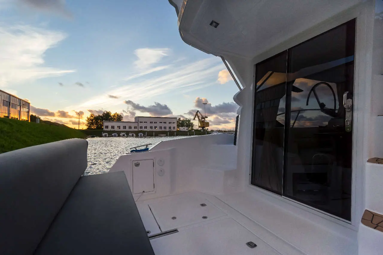 A boat deck overlooks a waterway at sunset with reflections on the glass door. A warehouse is visible in the background.