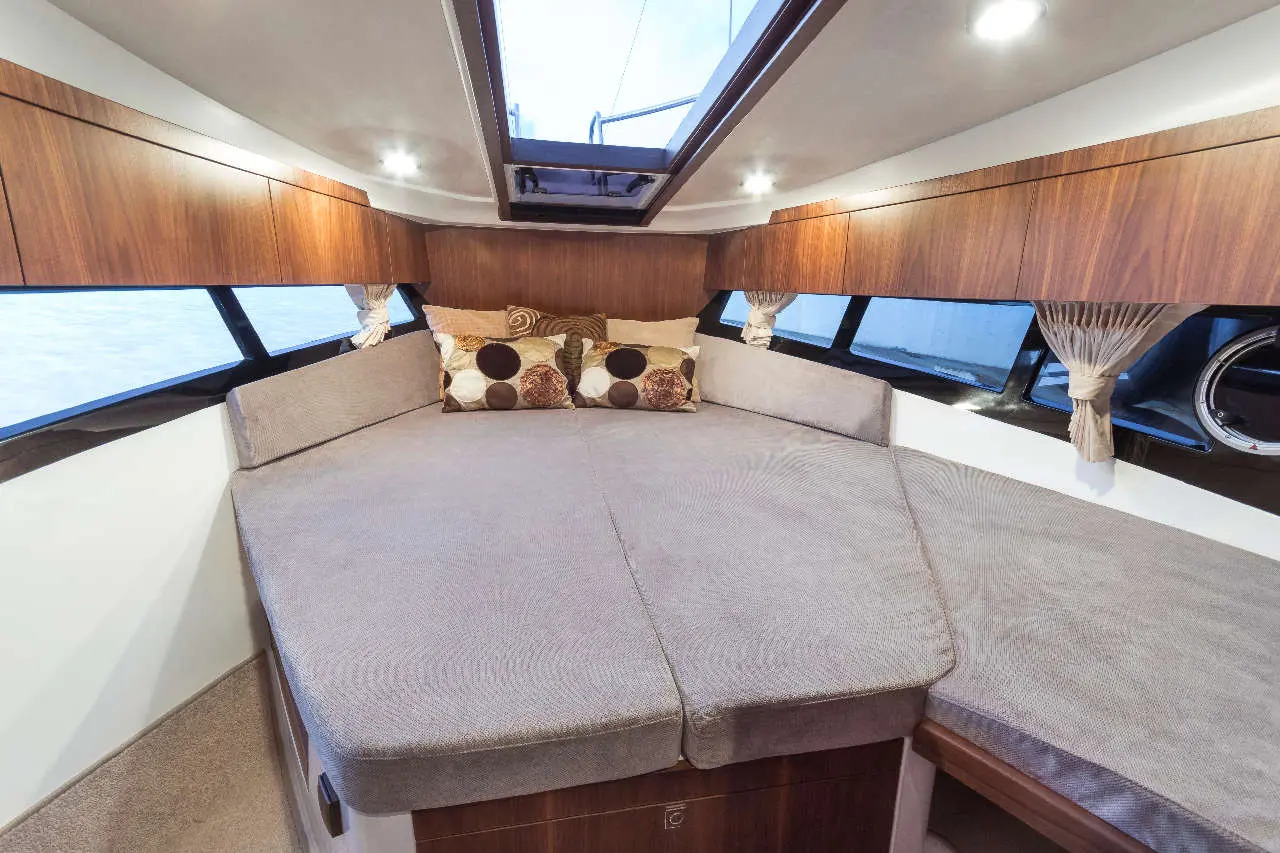 Modern boat interior featuring a spacious lounge area with cushioned seating, decorative pillows, and wooden cabinetry.