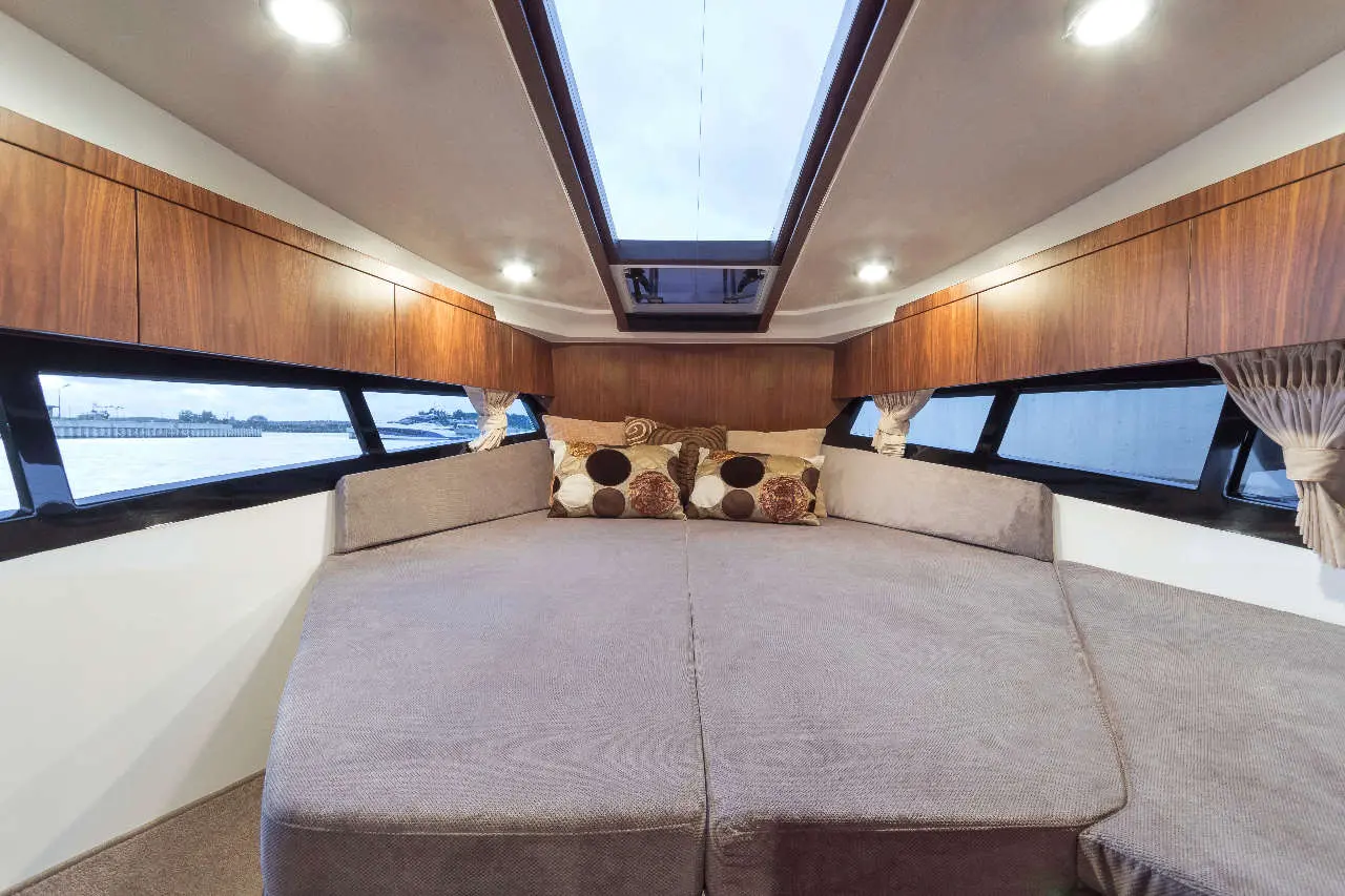 Modern boat interior featuring a large seating area, plush cushions, wooden cabinets, and natural light from skylights.