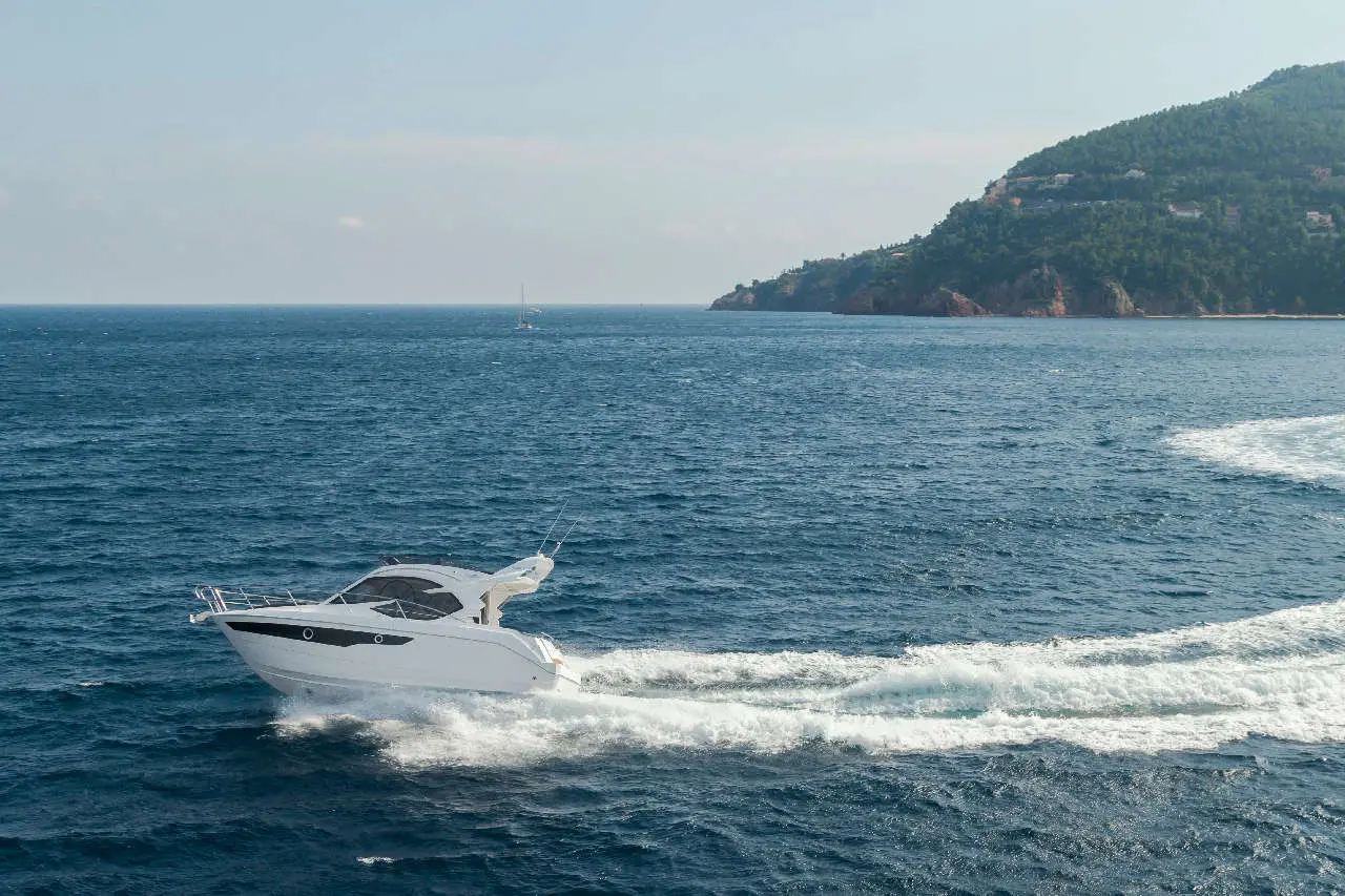 A motorboat glides through blue waters near a green coastal hill, creating a wake in the serene sea environment.