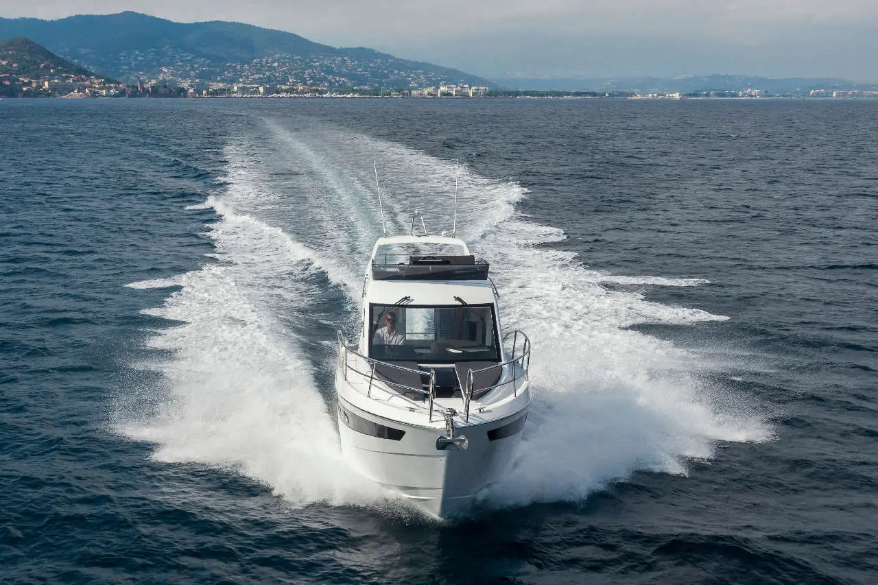 A white motorboat is cutting through waves on a calm sea, with a mountainous coastline in the background.