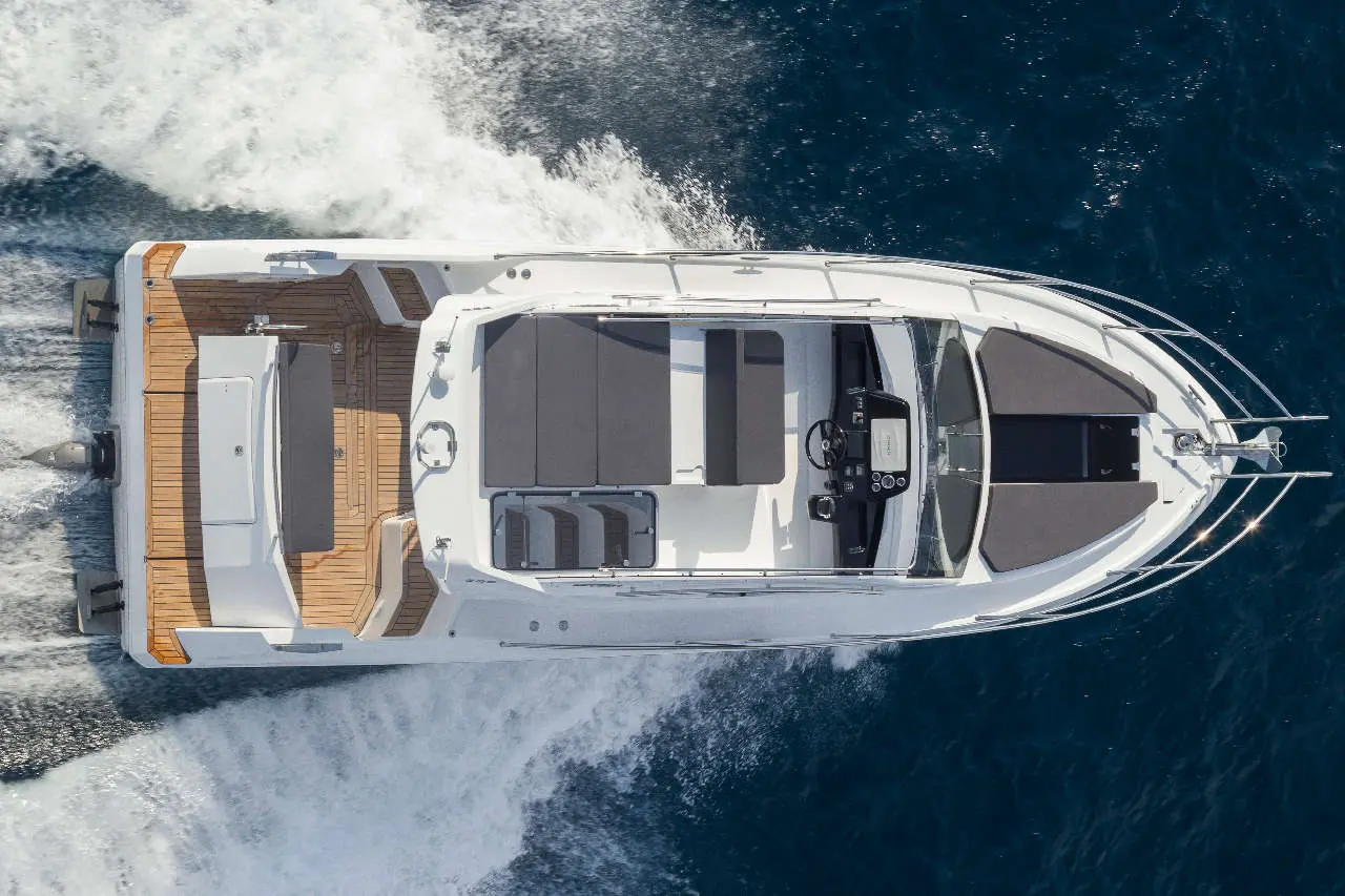 Aerial view of a sleek white motorboat with a spacious deck, cruising over deep blue waters, leaving a wake.