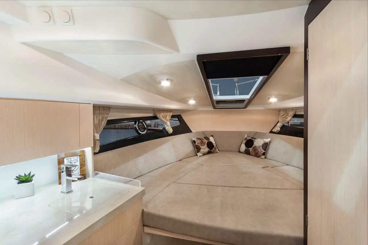 Interior of a modern boat cabin featuring a spacious circular bed, a sink area, decorative cushions, and large windows.