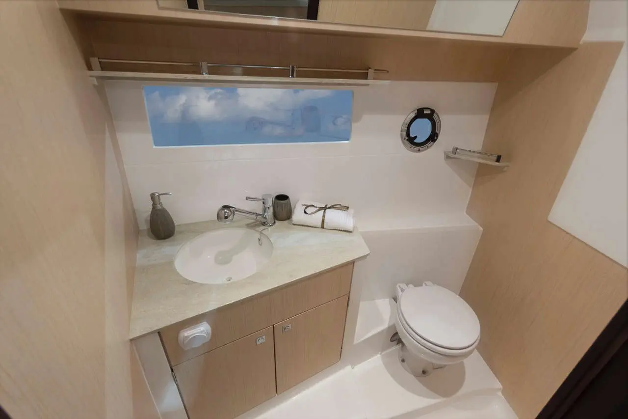 Compact bathroom featuring a sink, toilet, and storage, with a window showing clouds and a minimalist design.