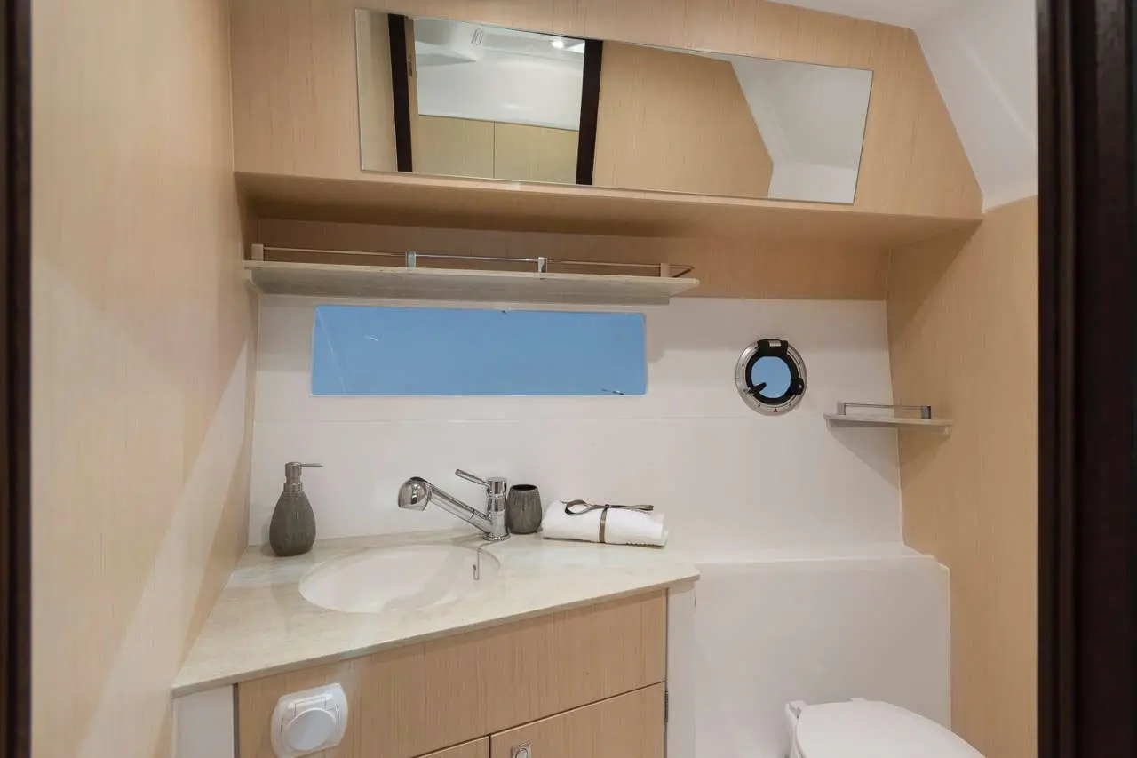 Modern boat bathroom featuring a sink, mirror, shelves, and porthole; includes a soap dispenser and rolled towels.