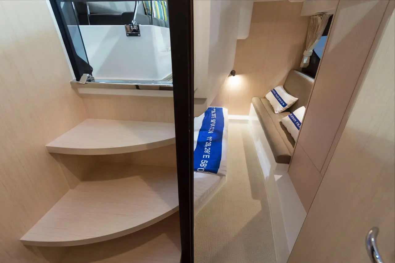 Interior view of a modern boat cabin, featuring curved wooden stairs, a sofa, and two pillows with 'SIMPLE PLEASURE' text.