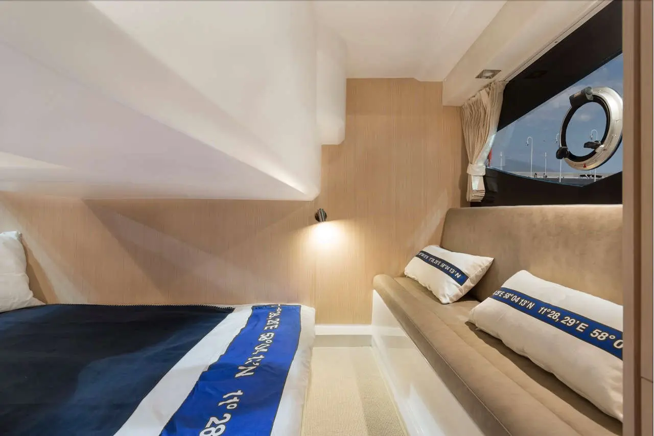 Stylish yacht cabin featuring a bed with black and white bedding, a beige sofa, and sea views through a round window.