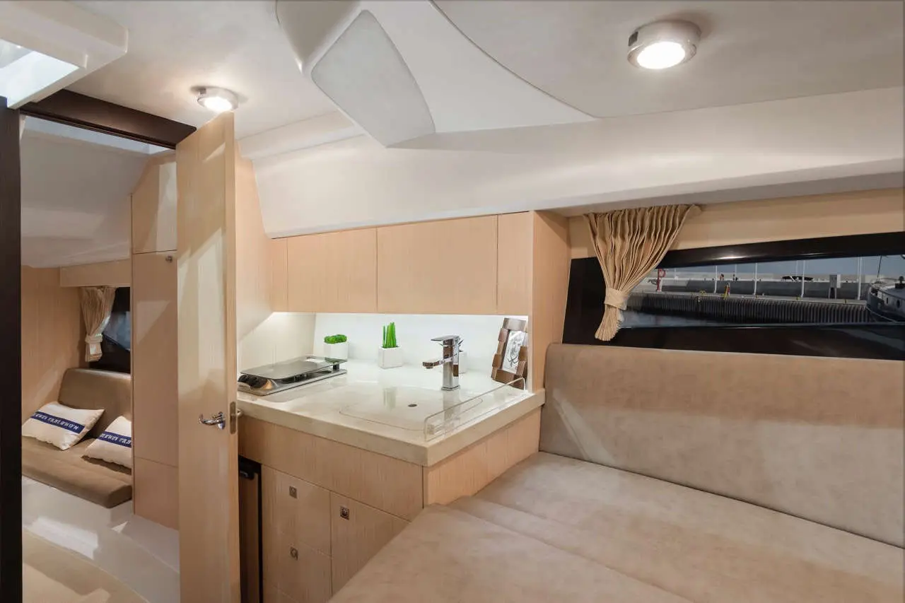 Interior view of a yacht's cabin featuring a kitchenette, seating area, and window with a view of boats outside.