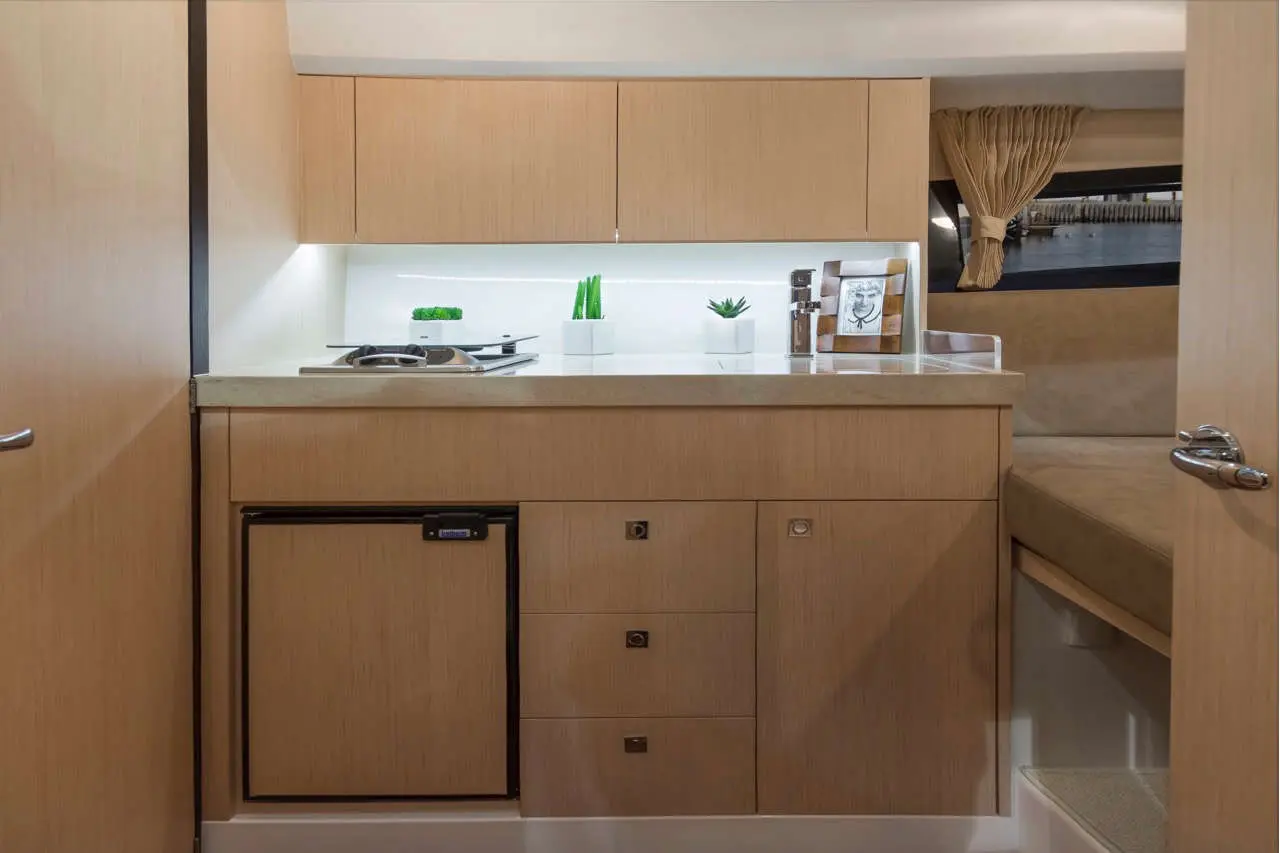 Modern yacht interior featuring a compact kitchen with a stove, refrigerator, and decorative plants on the countertop.