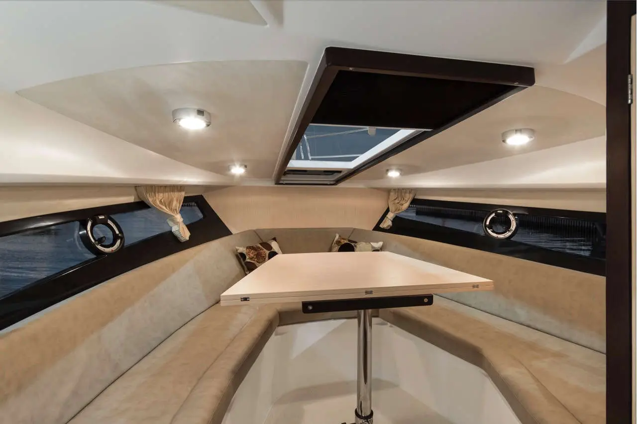 Modern boat interior featuring a table, curved bench seating, and windows with no visible text. Sleek design and lighting.