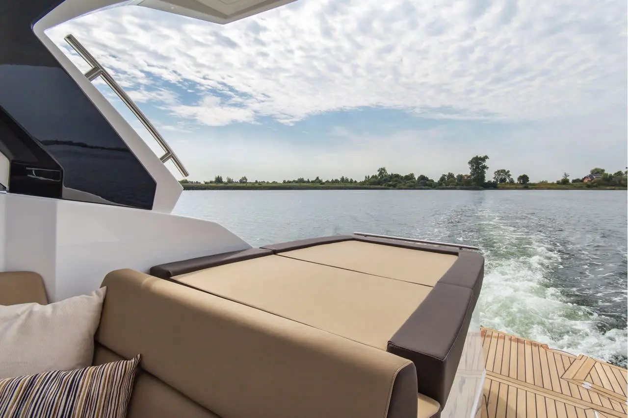 View from a yacht towards calm water, featuring a cushioned seating area and a cloudy sky in the background.