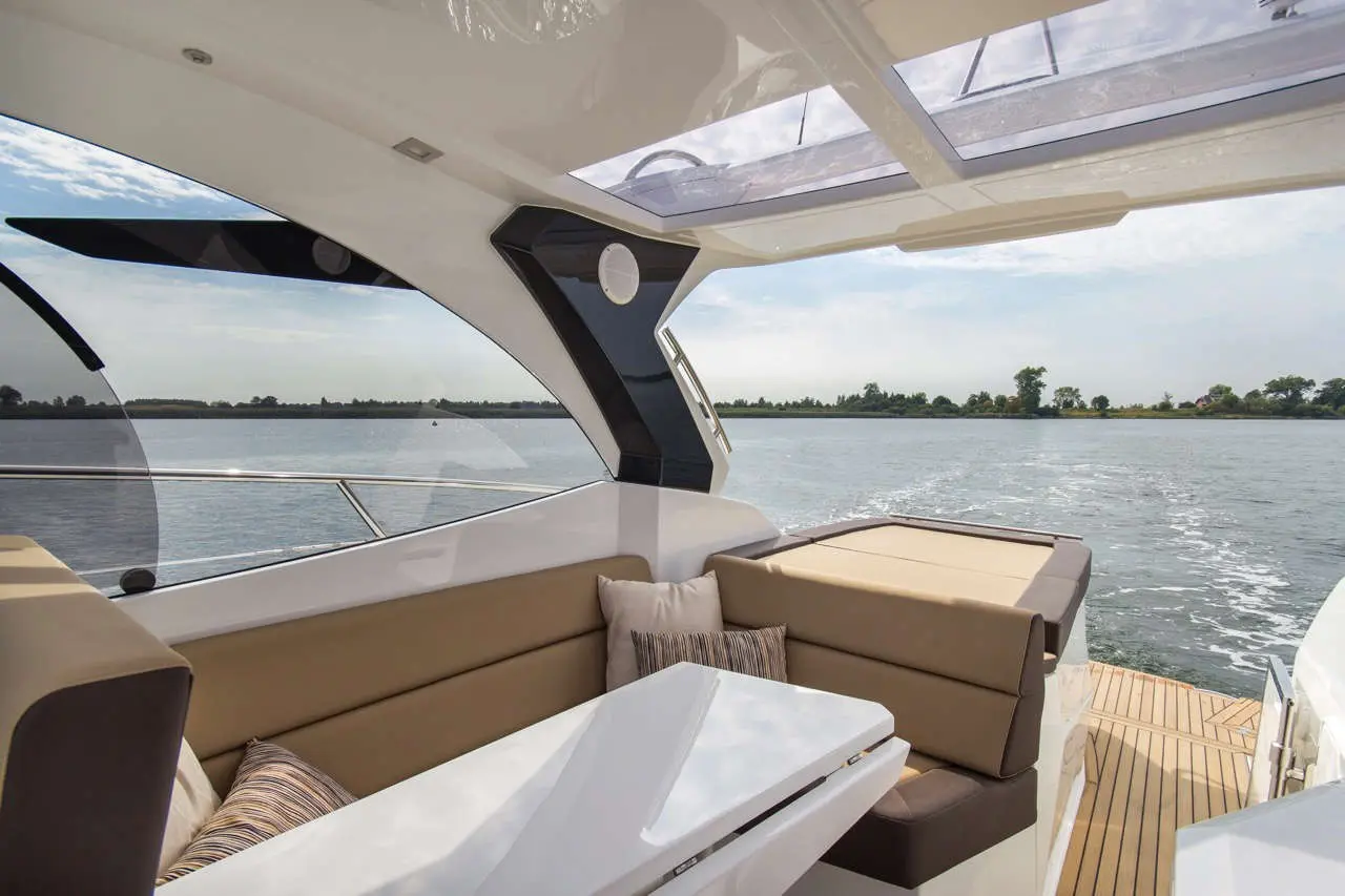 Luxury boat interior featuring a cushioned seating area, table, and panoramic views of a calm waterway under a clear sky.