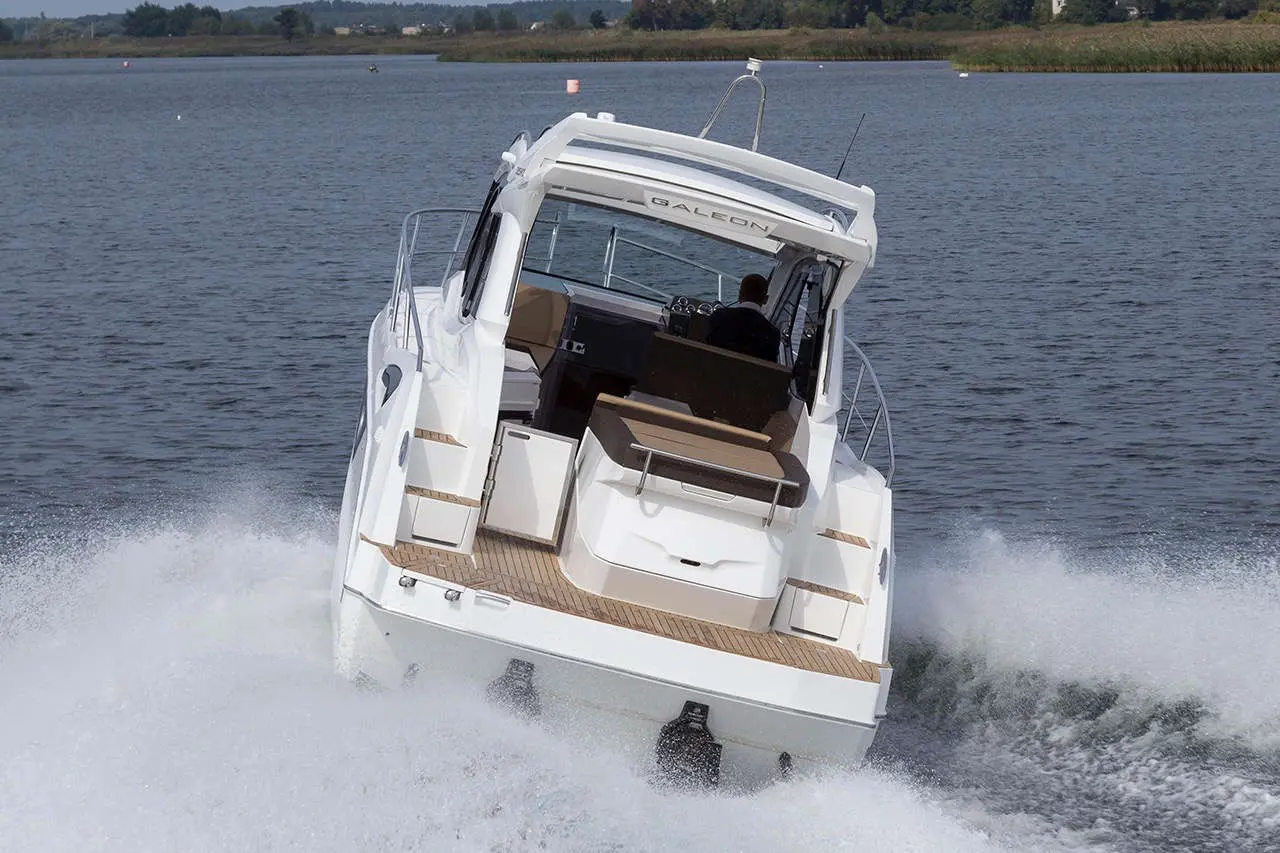 A Galia yacht with a cockpit and spacious seating, accelerating on a calm waterway against a scenic backdrop.