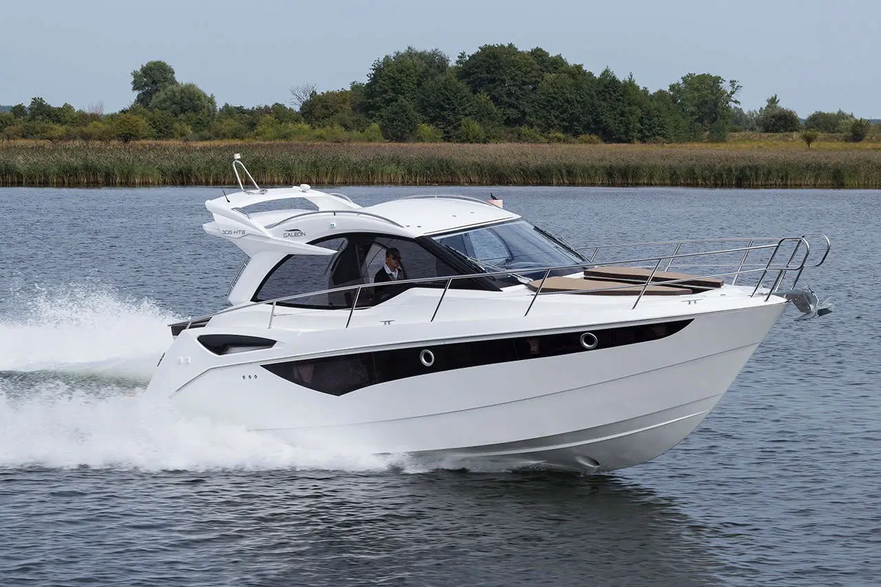 A Galeon 305 HTS motorboat speeds across calm water, with greenery lining the shore in the background.