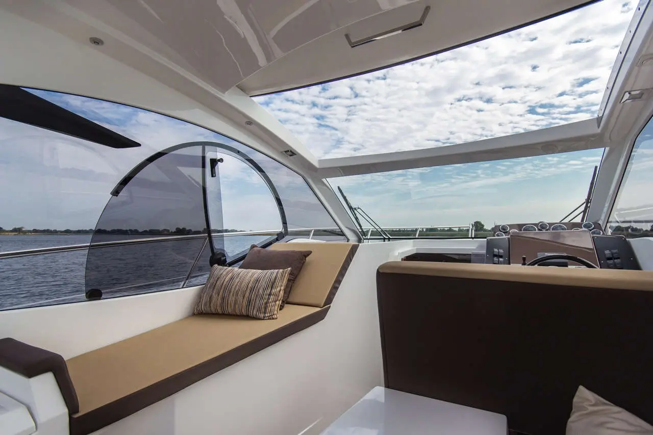 Luxury boat interior featuring a spacious seating area and modern helm, with scenic views of water and clouds through large windows.