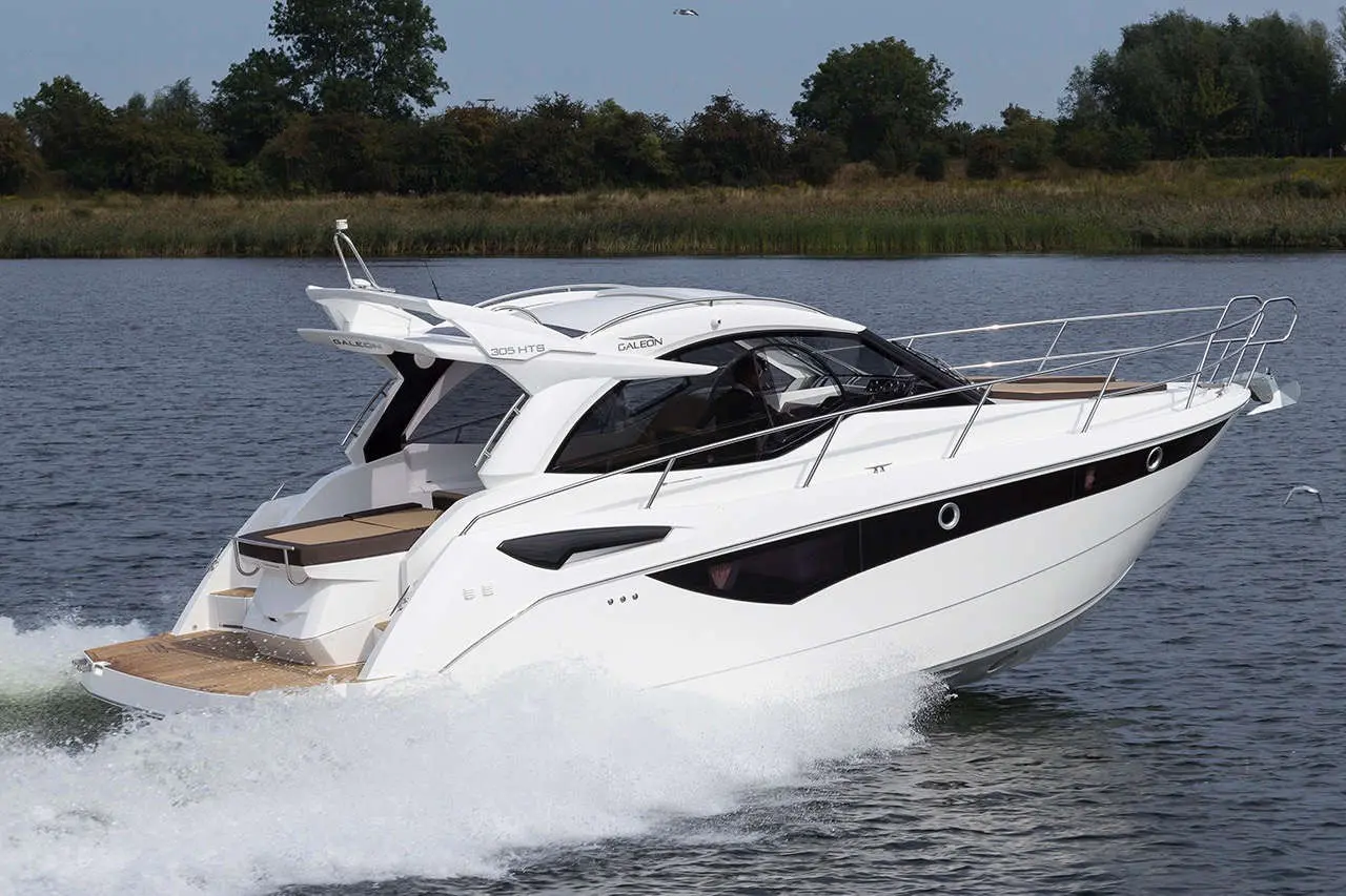 A sleek white motorboat, Galeon 305 HTS, cruising over rippling water with greenery in the background.