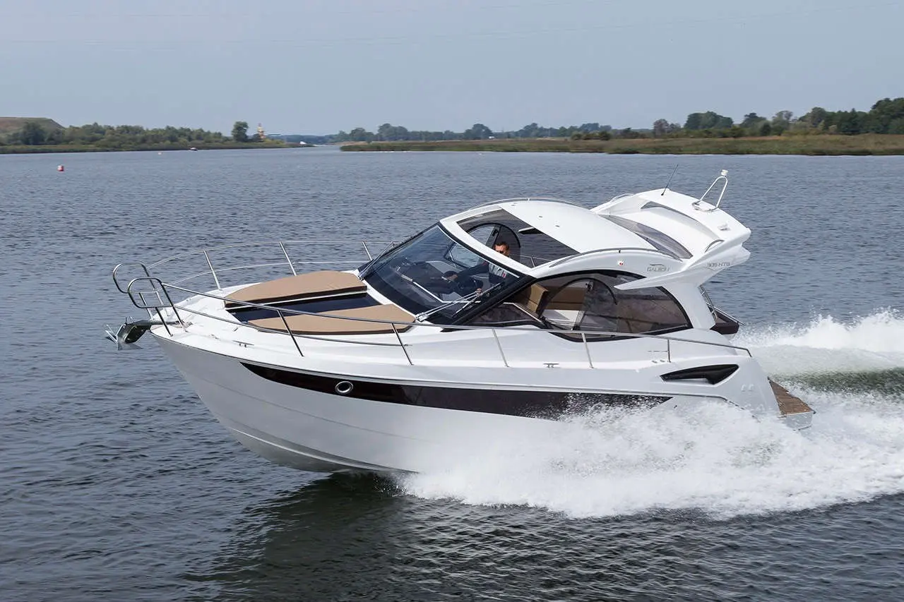 A white motorboat speeds across a calm river, creating waves behind it under a clear sky.