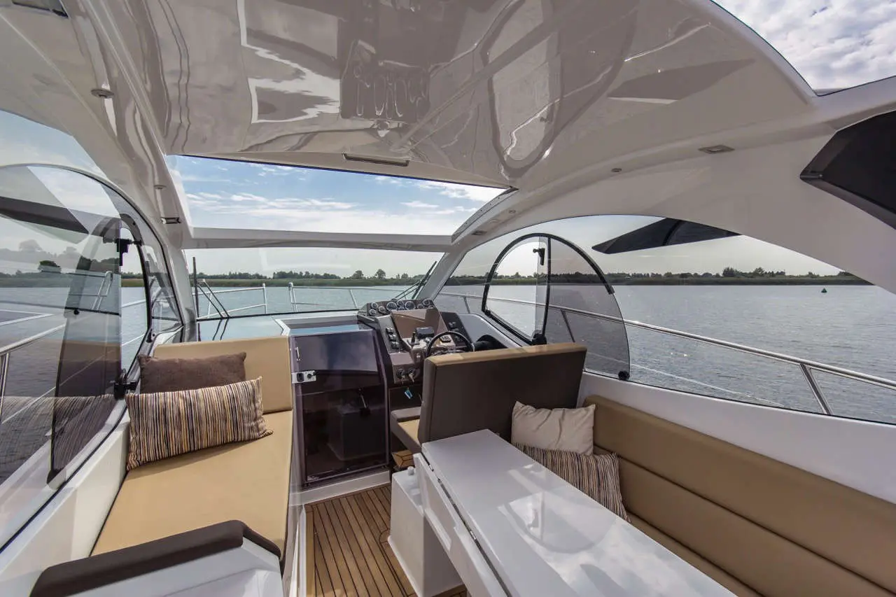 Luxury boat interior featuring a spacious seating area, modern controls, and views of calm waters and shoreline.