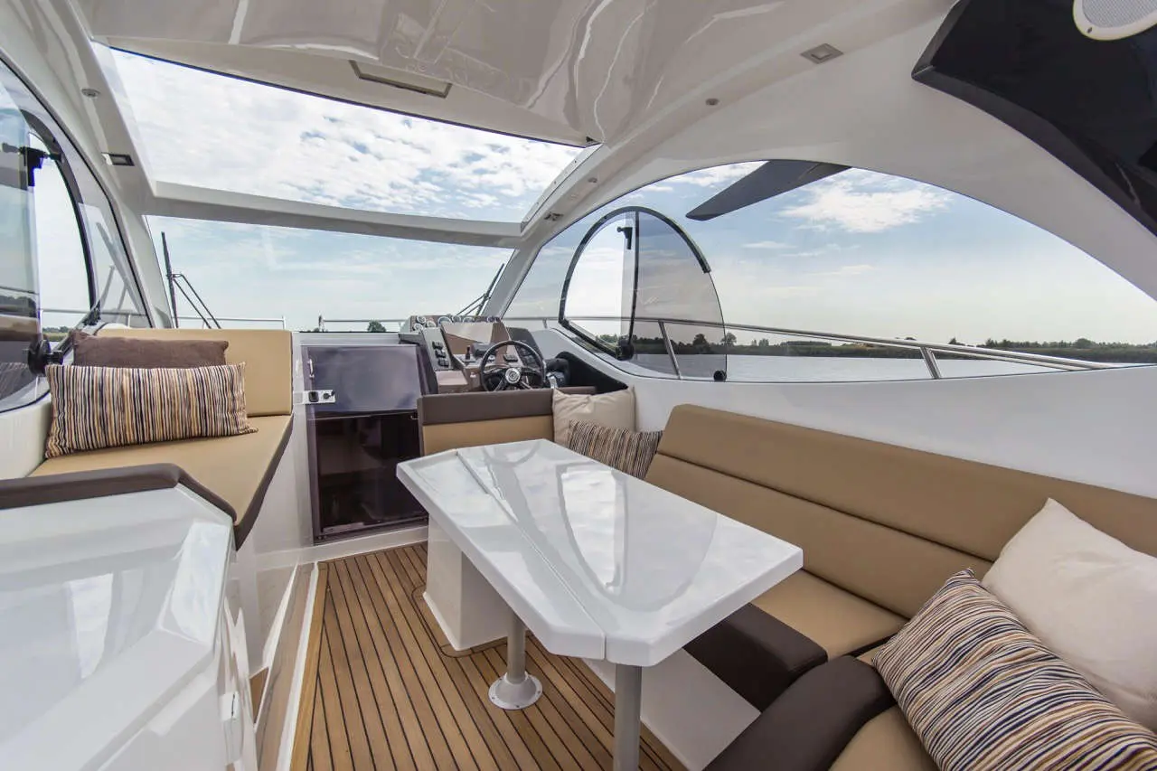 Modern yacht interior featuring a seating area, sleek table, and panoramic windows overlooking a serene water view.