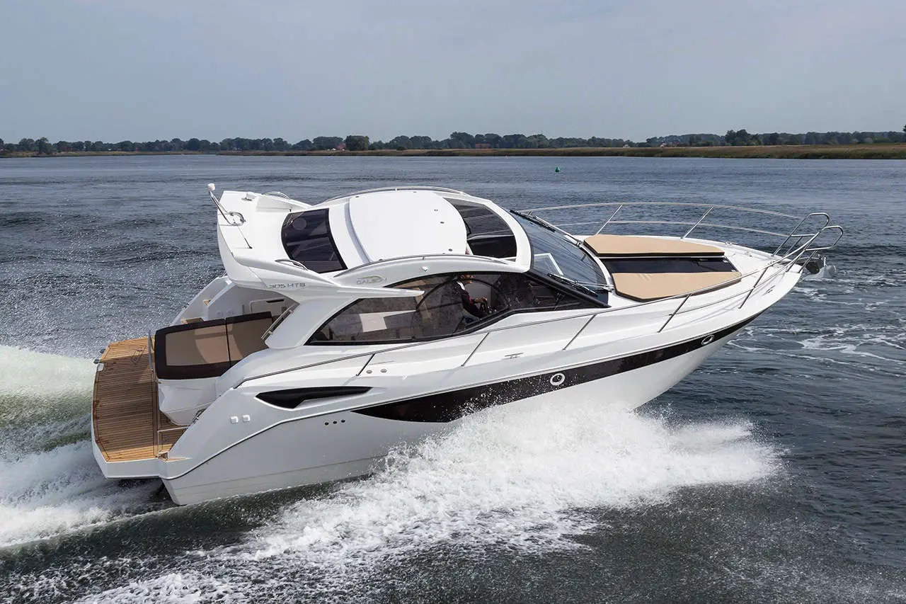A sleek motorboat glides through calm water, creating white spray, with a scenic shoreline in the background.
