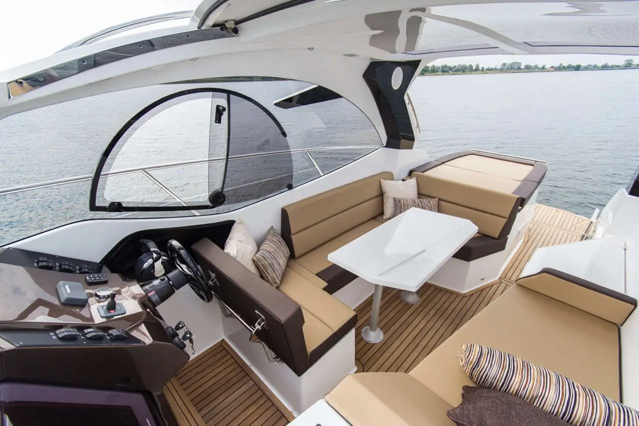 Interior of a modern yacht featuring a stylish helm, cushioned seating, and a sleek table overlooking the water.