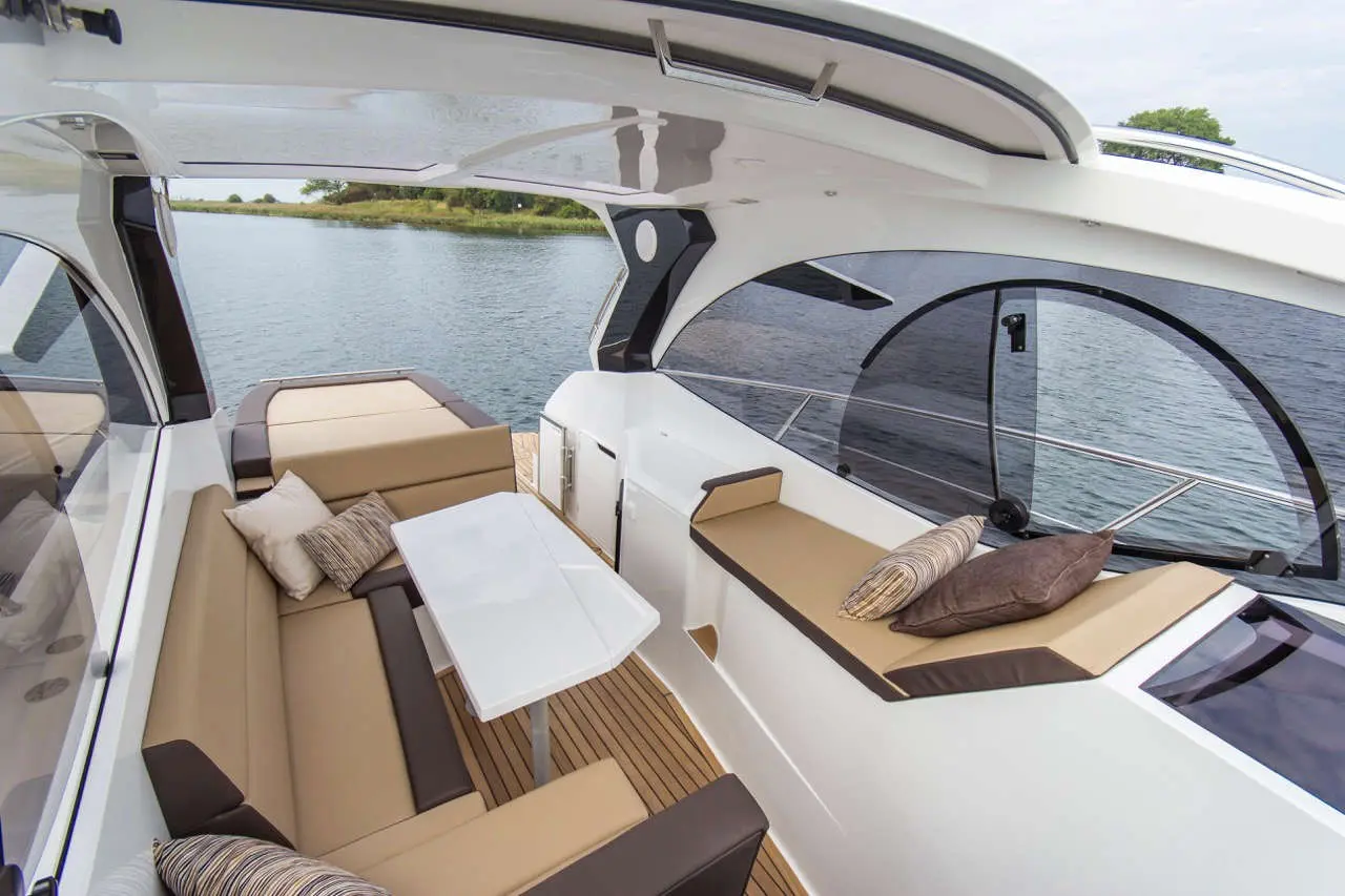 Interior of a modern boat featuring plush seating, a white table, and a view of calm water and greenery outside.