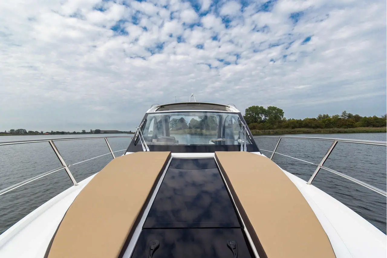 View from the bow of a luxury boat featuring cushioned seating, a panoramic windshield, and a serene waterway background.