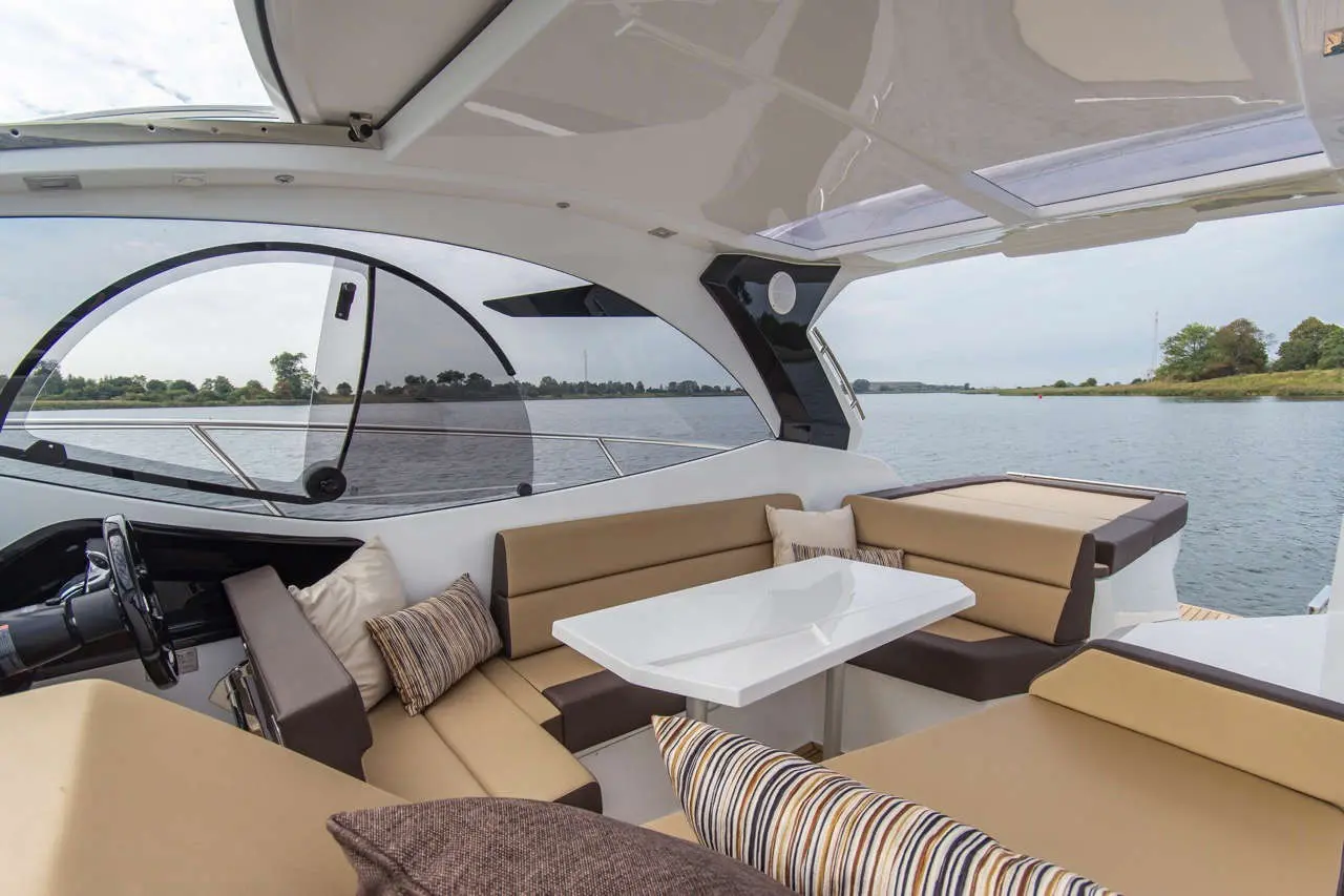Luxurious boat interior featuring a seating area, table, and panoramic windows overlooking a peaceful waterway.