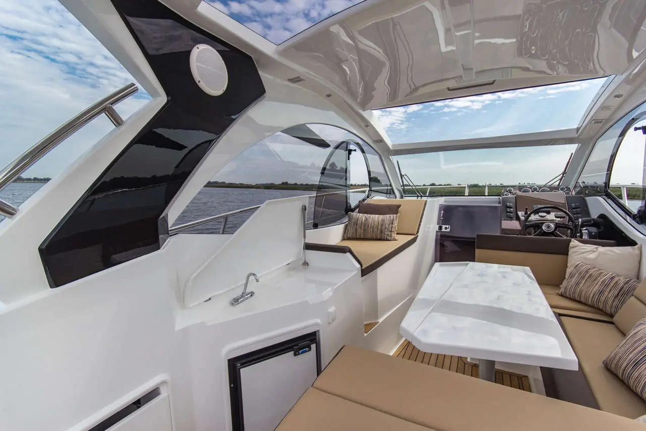 Stylish indoor seating area of a boat with a dining table, soft cushions, and panoramic windows overlooking water.