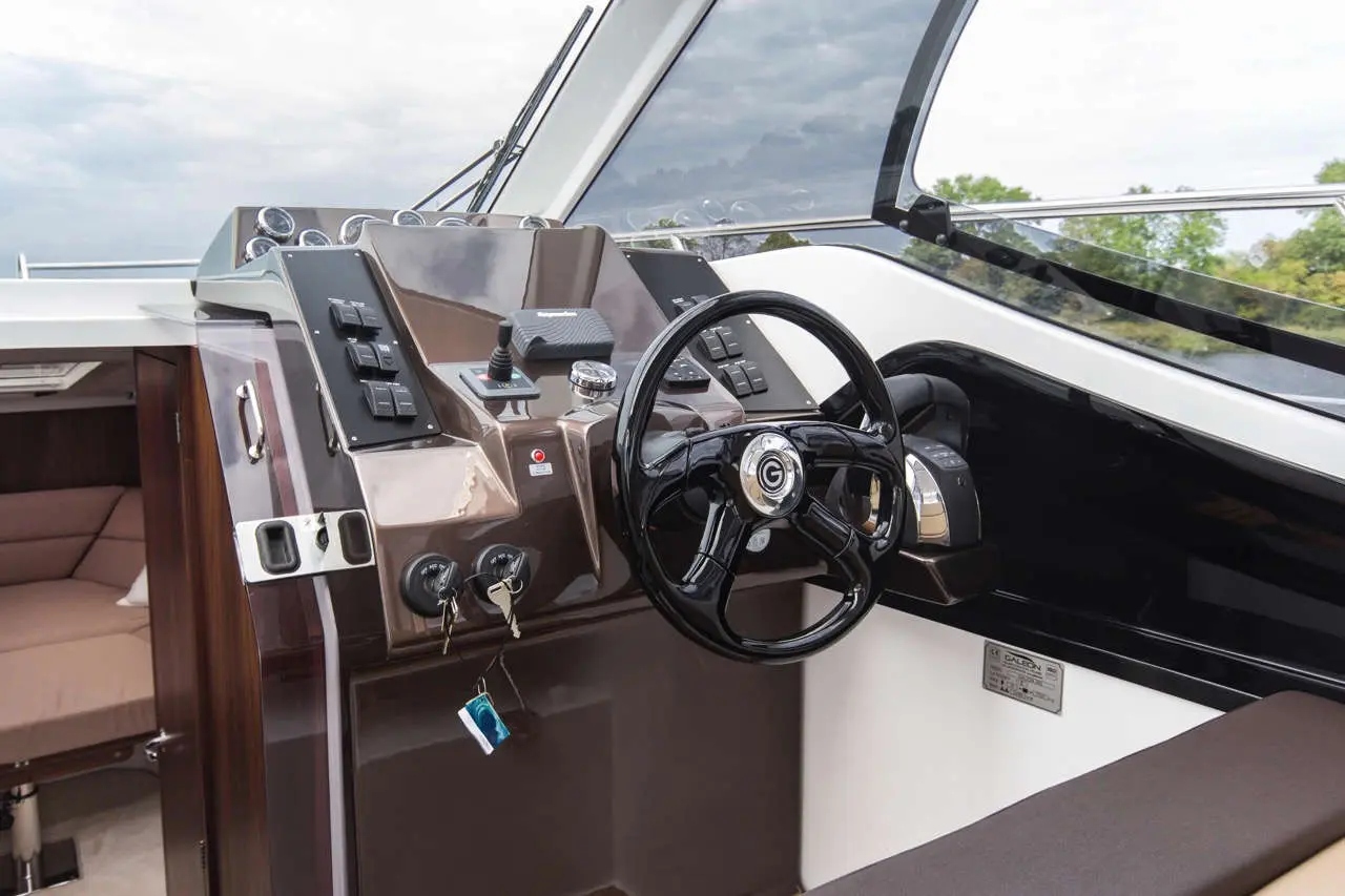 Luxury boat cockpit featuring a steering wheel, control switches, and visibility through large windows.