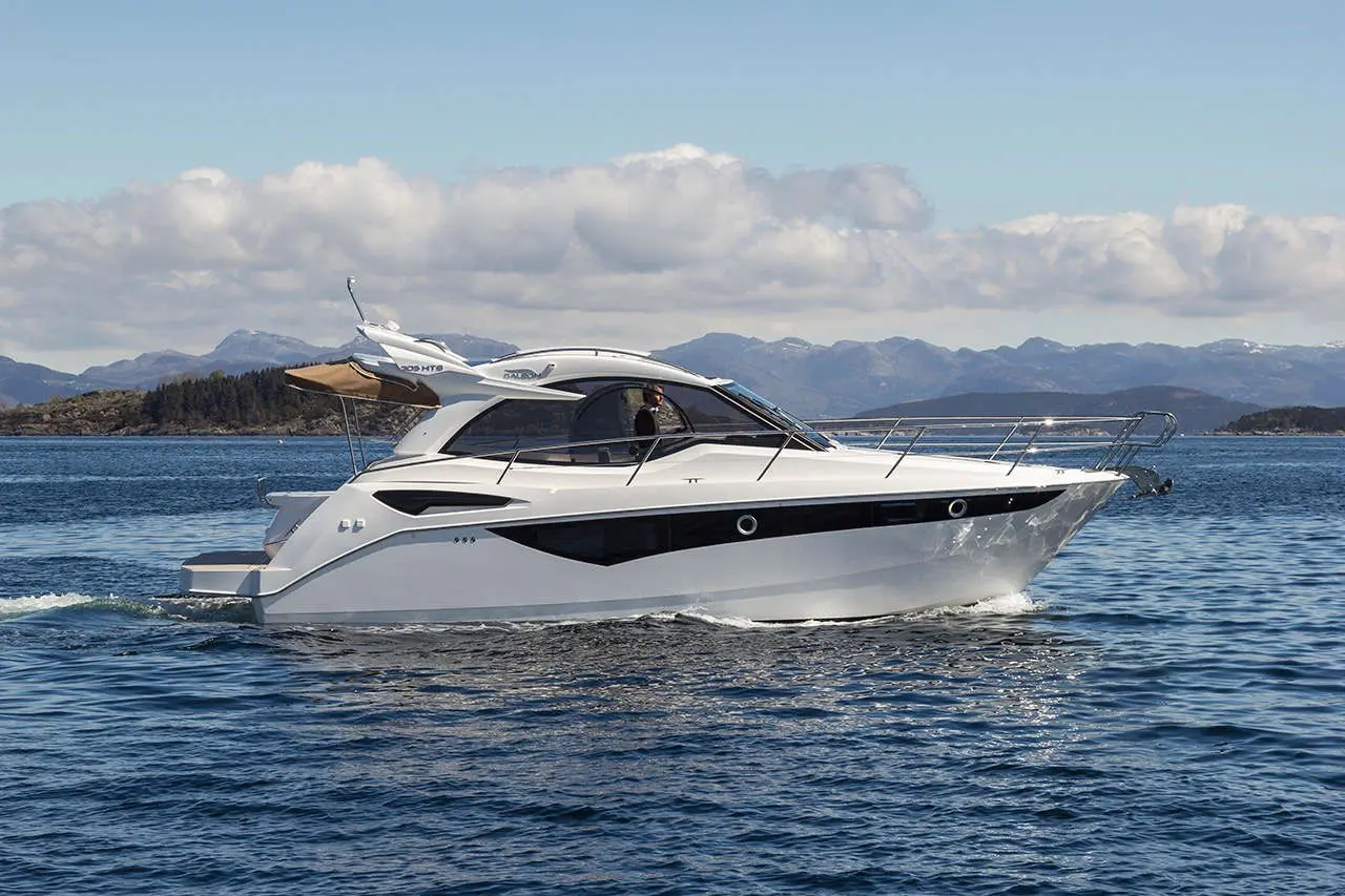 A sleek white motorboat cruising on calm waters, with mountains visible in the background under a partly cloudy sky.