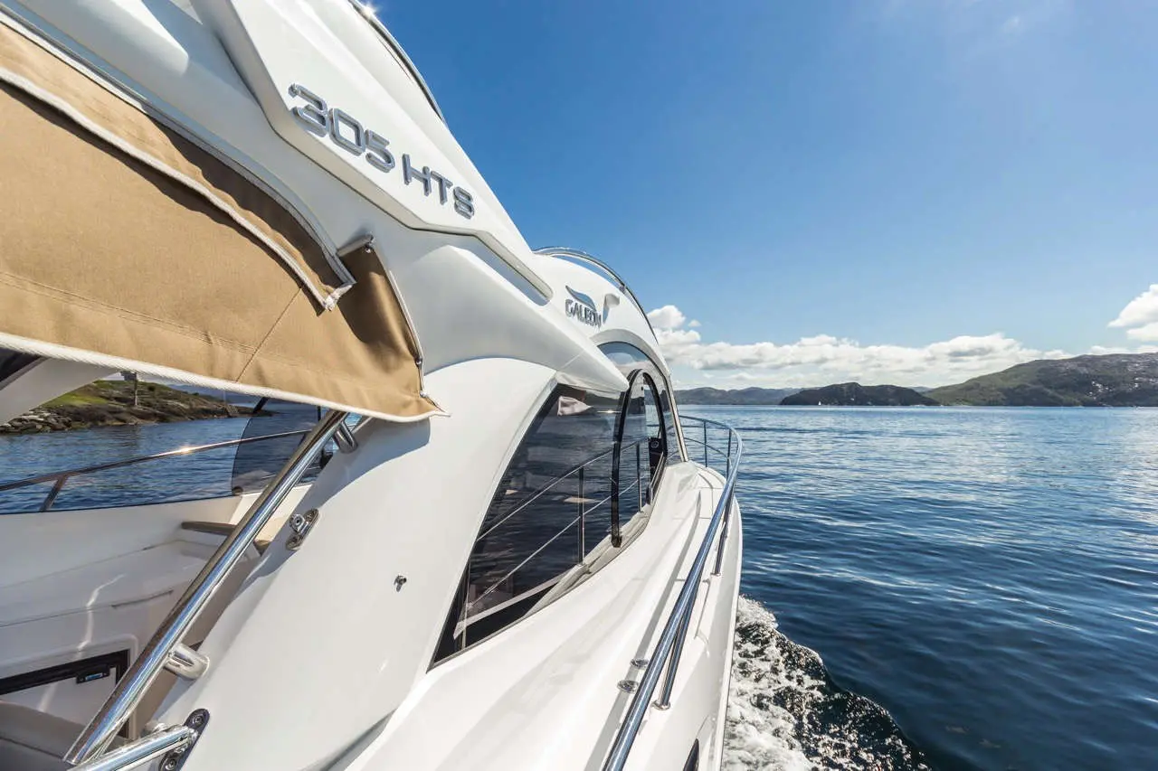 A white motorboat, model 305 HTS, cruising on calm waters with scenic hills and a clear blue sky in the background.