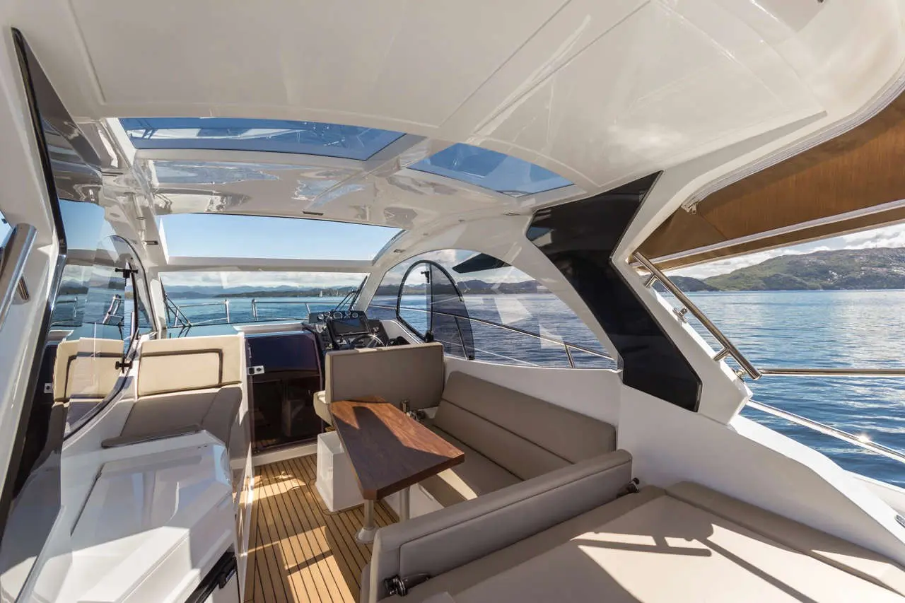 Luxury yacht interior with a wooden table, spacious seating, large windows, and views of water and mountains.