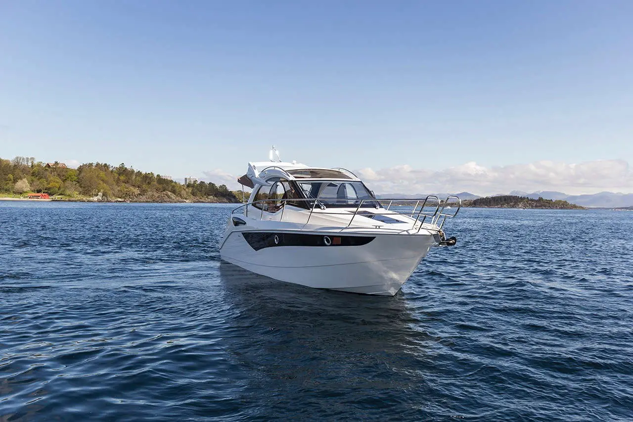 A white motorboat glides across calm waters, set against a scenic backdrop of green hills under a clear blue sky.