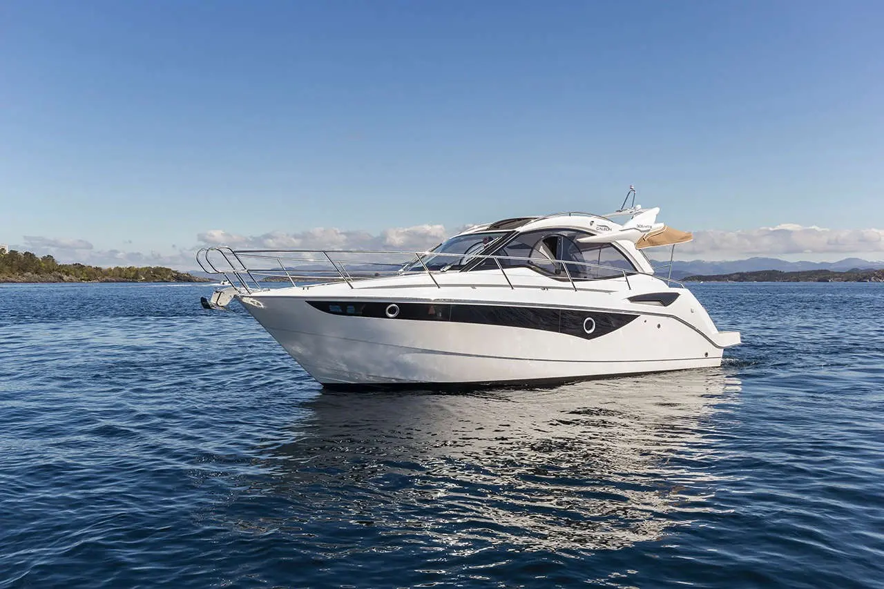 A sleek white motorboat with a black stripe, anchored on calm water against a clear blue sky and distant hills.