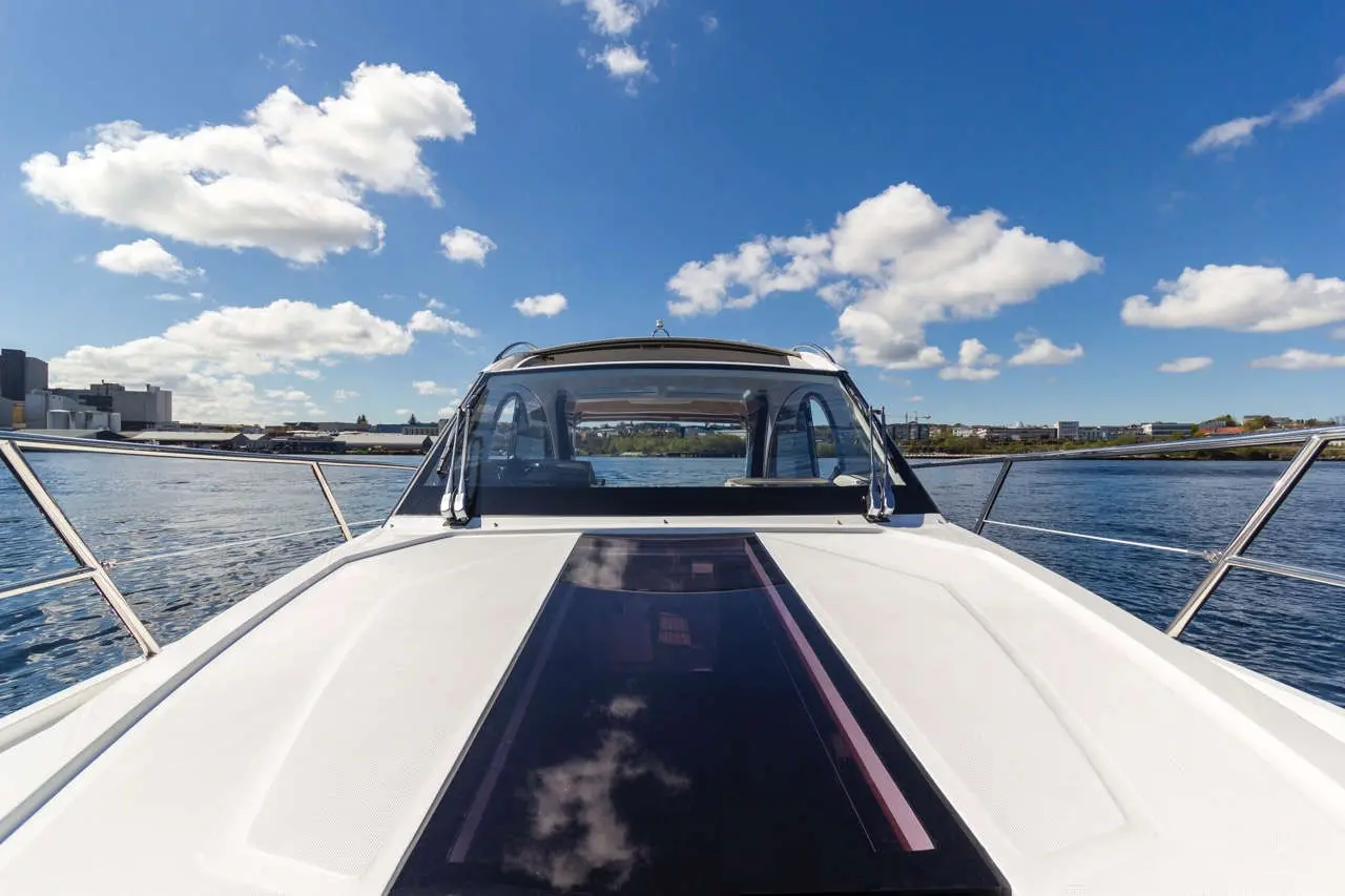 View from the helm of a boat, showcasing a wide blue sky with clouds and reflections on the water, cityscape in the background.