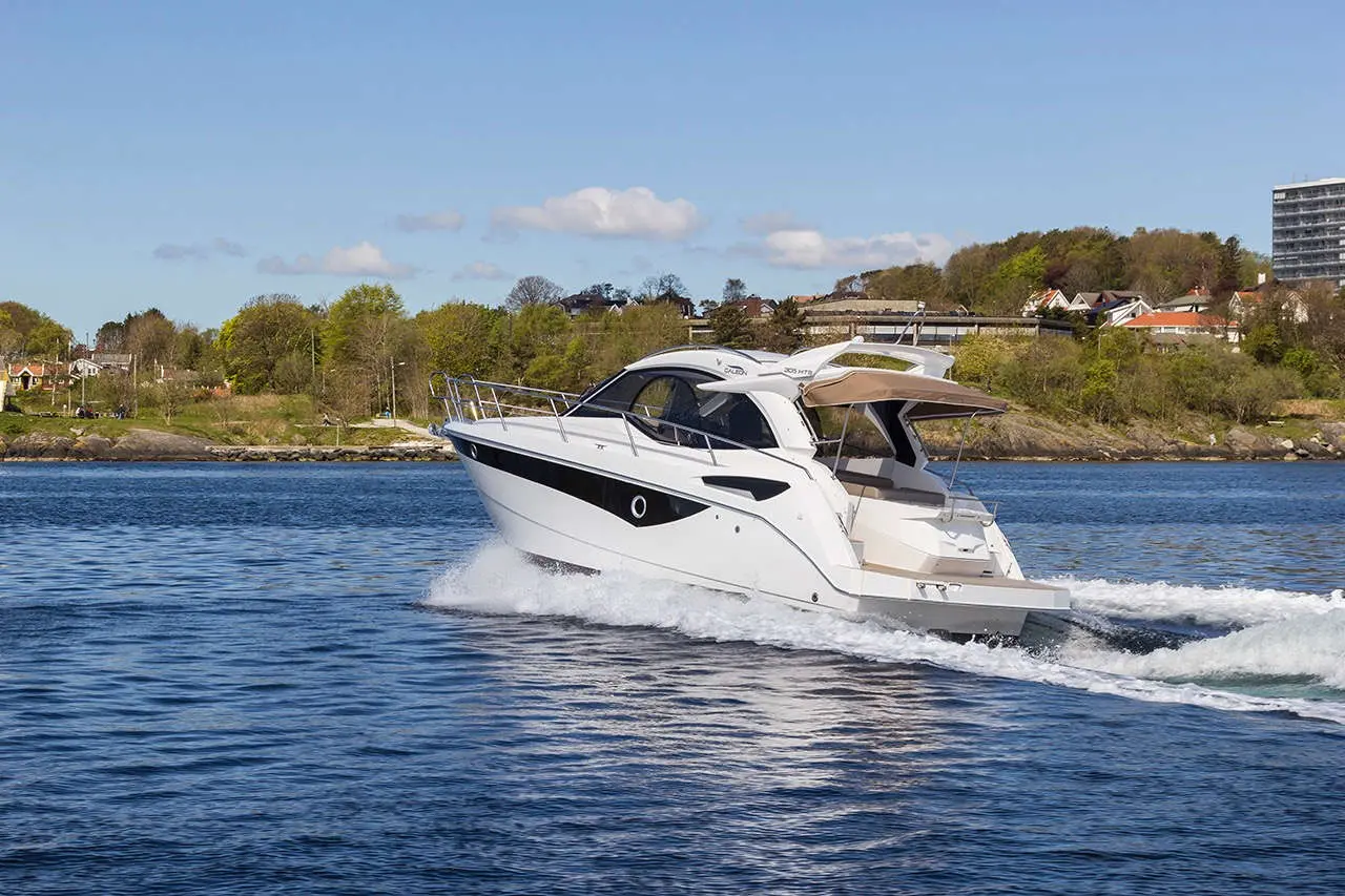 White motorboat cruising in calm water, surrounded by greenery and buildings under a clear blue sky.