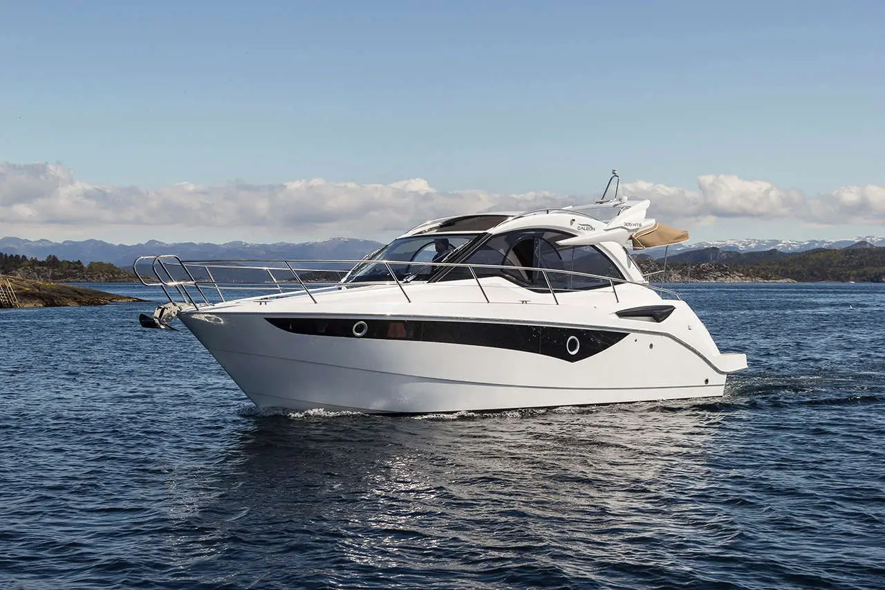A sleek white motorboat with black accents cruising on calm waters, surrounded by mountains and a clear blue sky.