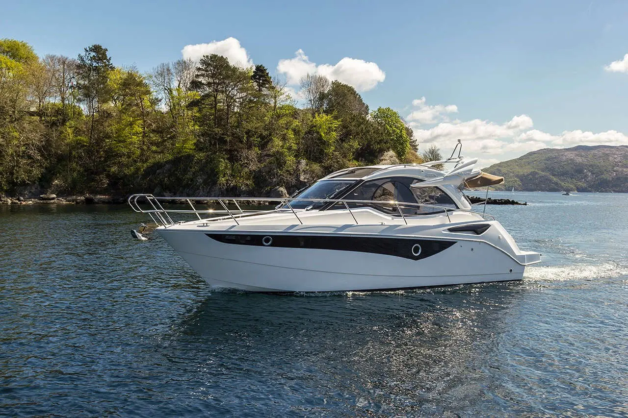 A sleek white motorboat cruising on a calm lake, framed by lush green trees and a clear blue sky.
