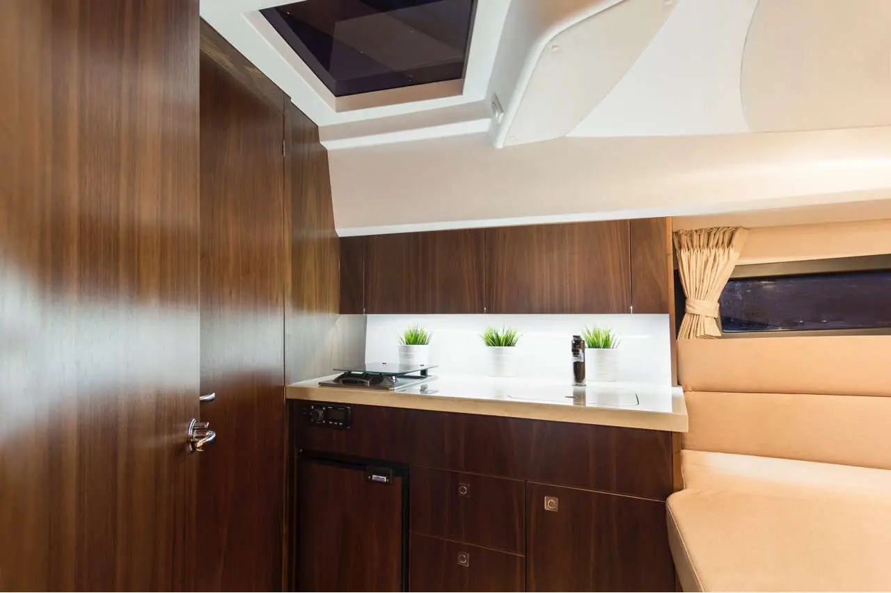 Modern yacht kitchen featuring wooden cabinetry, a sink, stovetop, and small plants under ambient lighting.