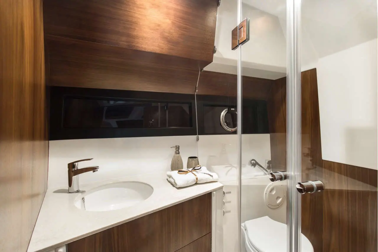 Modern yacht bathroom featuring a shower, sink, wooden cabinetry, and neatly arranged towels on the countertop.